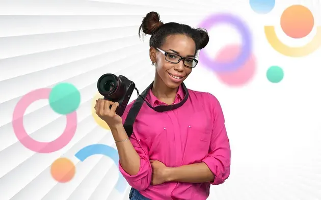 Une femme en chemise rose tient un appareil photo.