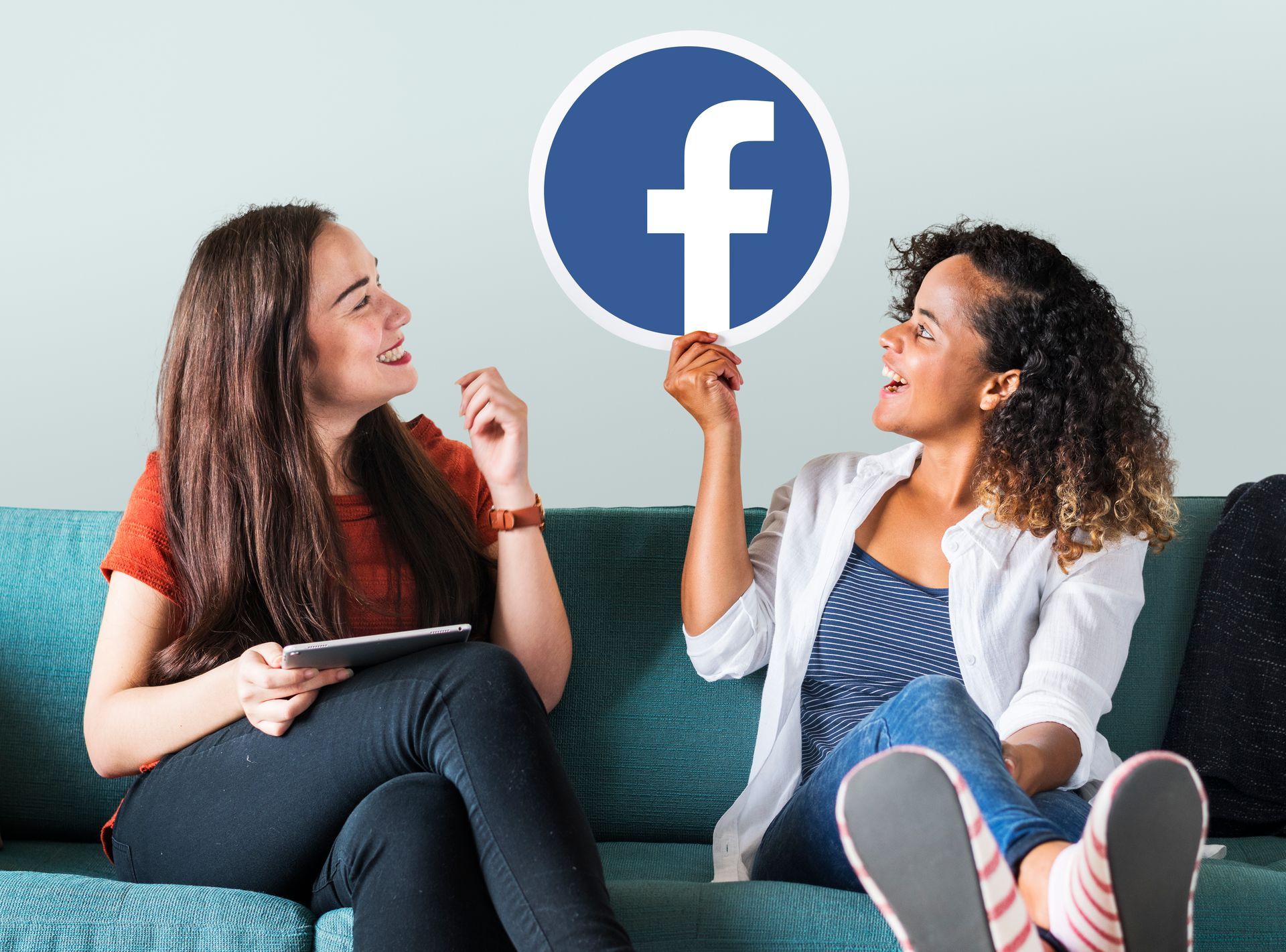 Deux femmes sont assises sur un canapé tenant une pancarte Facebook.