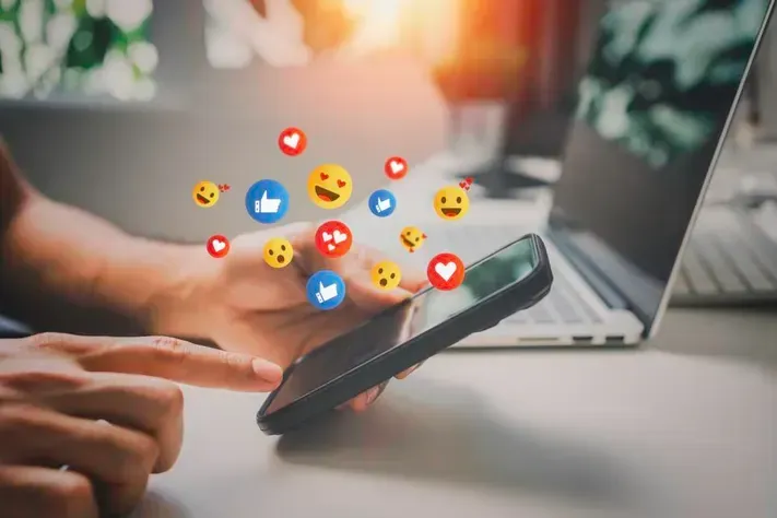 Une personne utilise un téléphone portable devant un ordinateur portable.