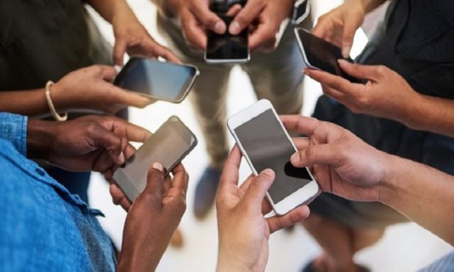 Un groupe de personnes debout en cercle, chacune tenant et utilisant son propre smartphone.