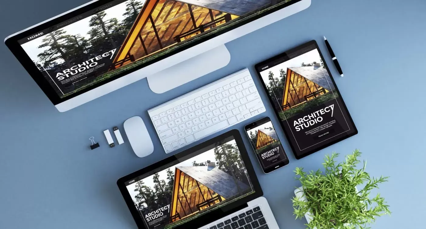 Un espace de travail montrant un ordinateur, un ordinateur portable, une tablette et un smartphone affichant le même site web d'architecture sur un bureau bleu.