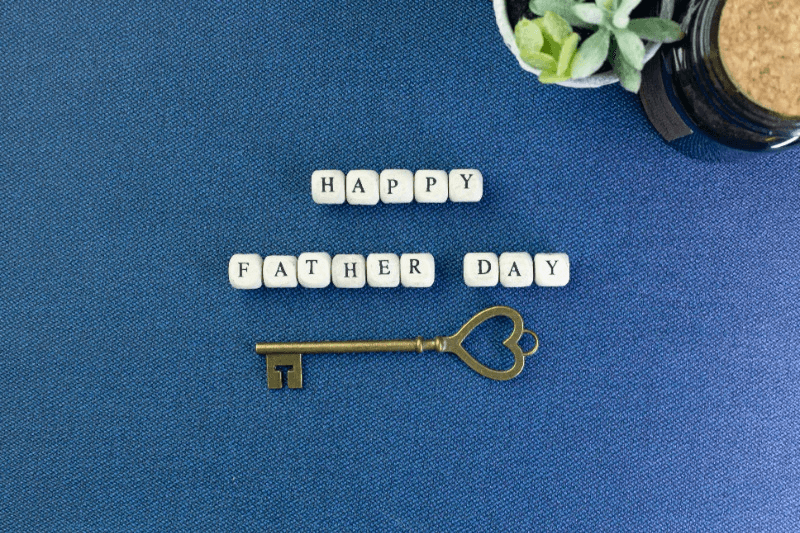 Un message de bonne fête des pères avec une clé sur une surface bleue.