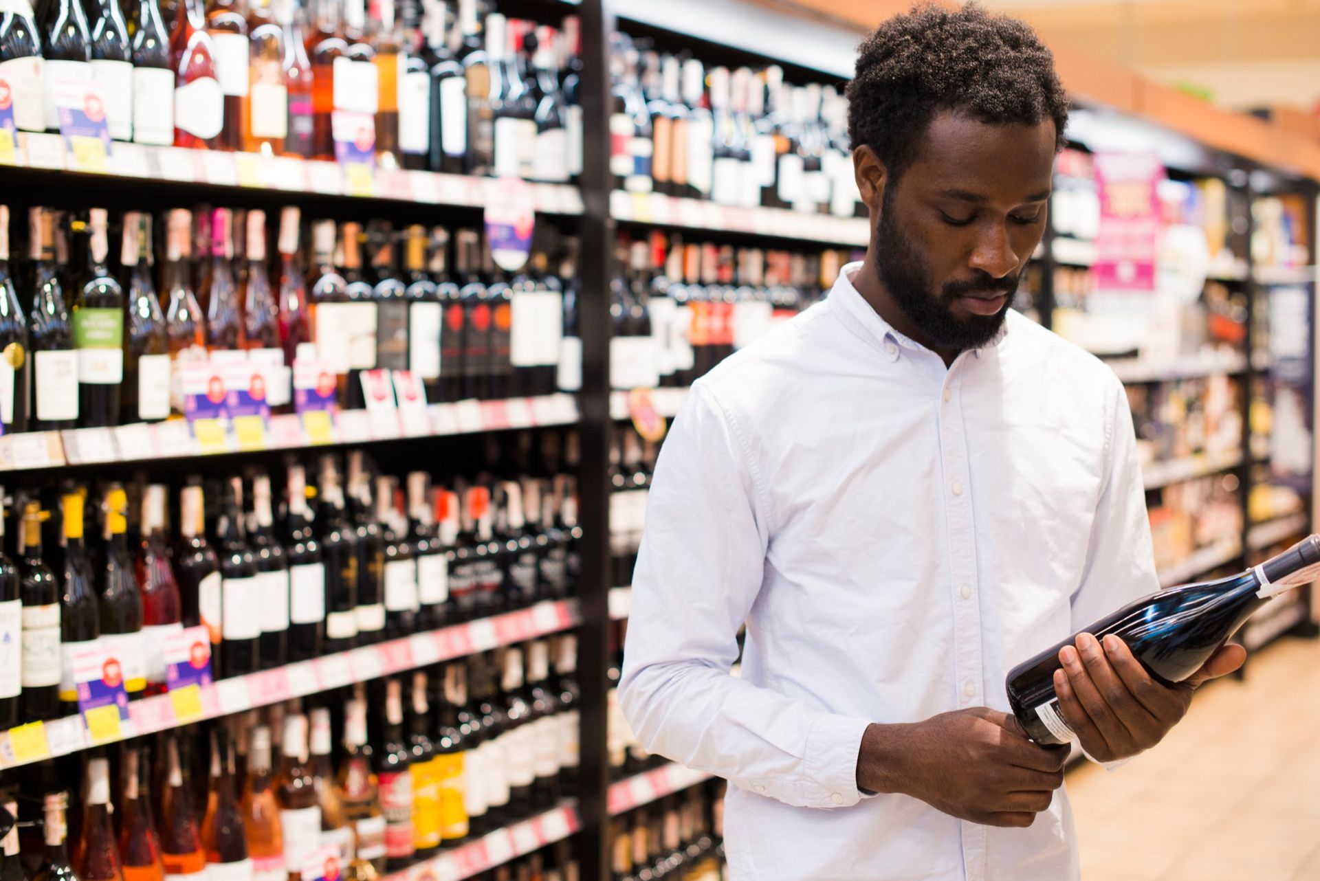 Un homme regarde une bouteille de vin dans une épicerie.