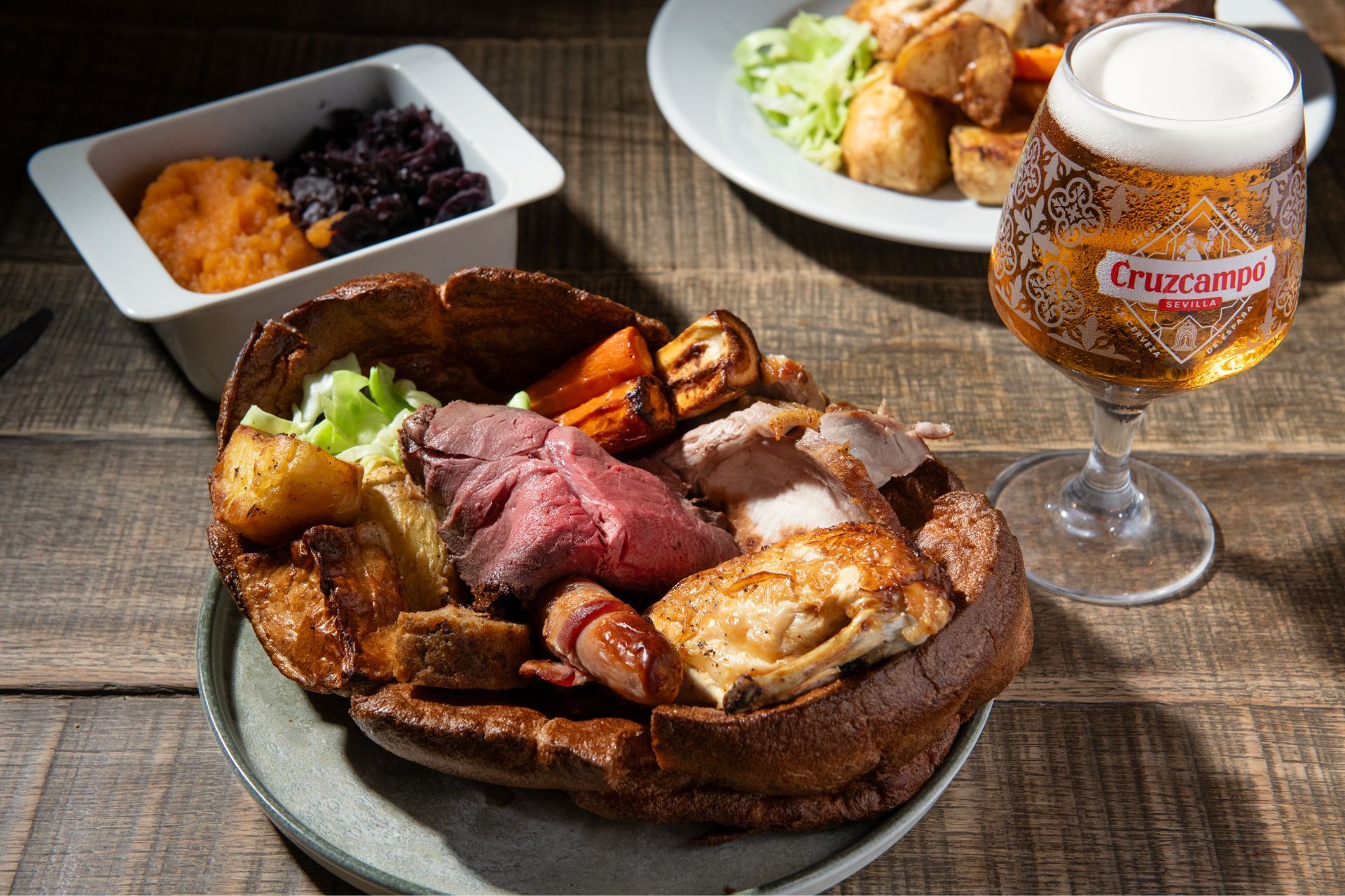 Roast pork on a wire rack in a kitchen oven, browned and glazed with sliced potatoes nearby