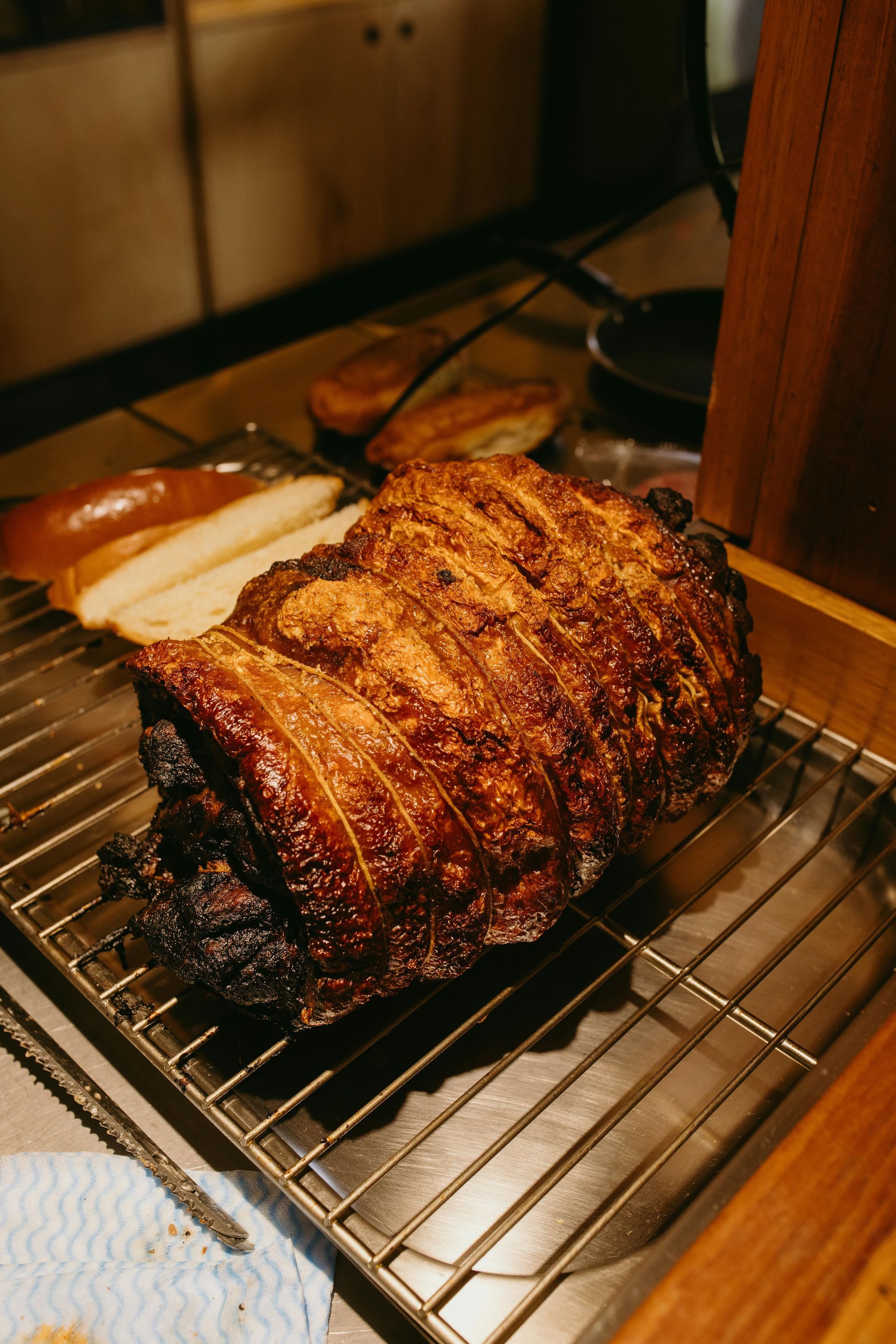Roast pork on a wire rack in a kitchen oven, browned and glazed with sliced potatoes nearby