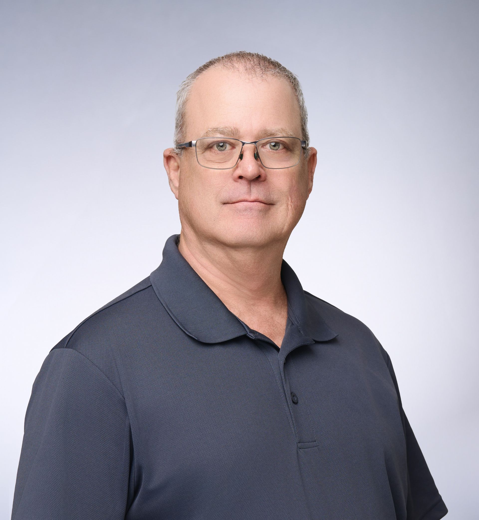 A man wearing glasses and a blue shirt is standing in front of a white background.