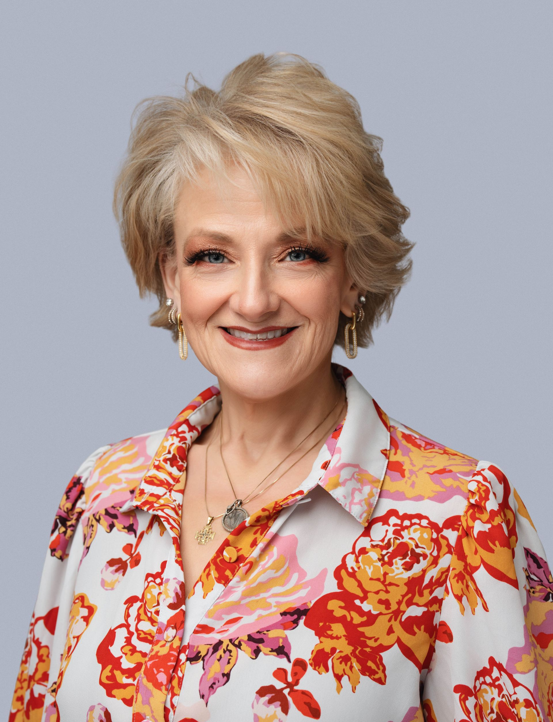 Smiling woman in a floral blouse against a gray background