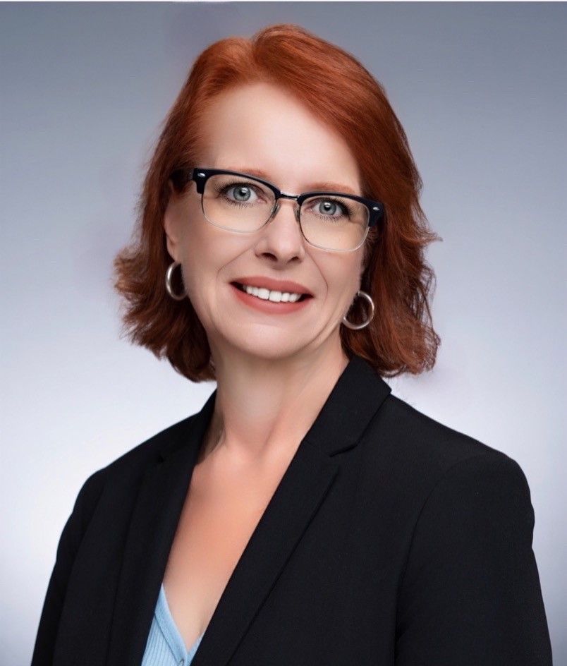 A woman with red hair and glasses is wearing a black shirt.