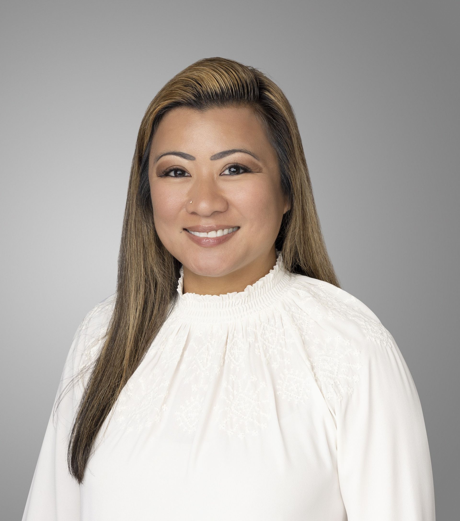 Honileth Virani smiling in a white blouse against a gray studio background