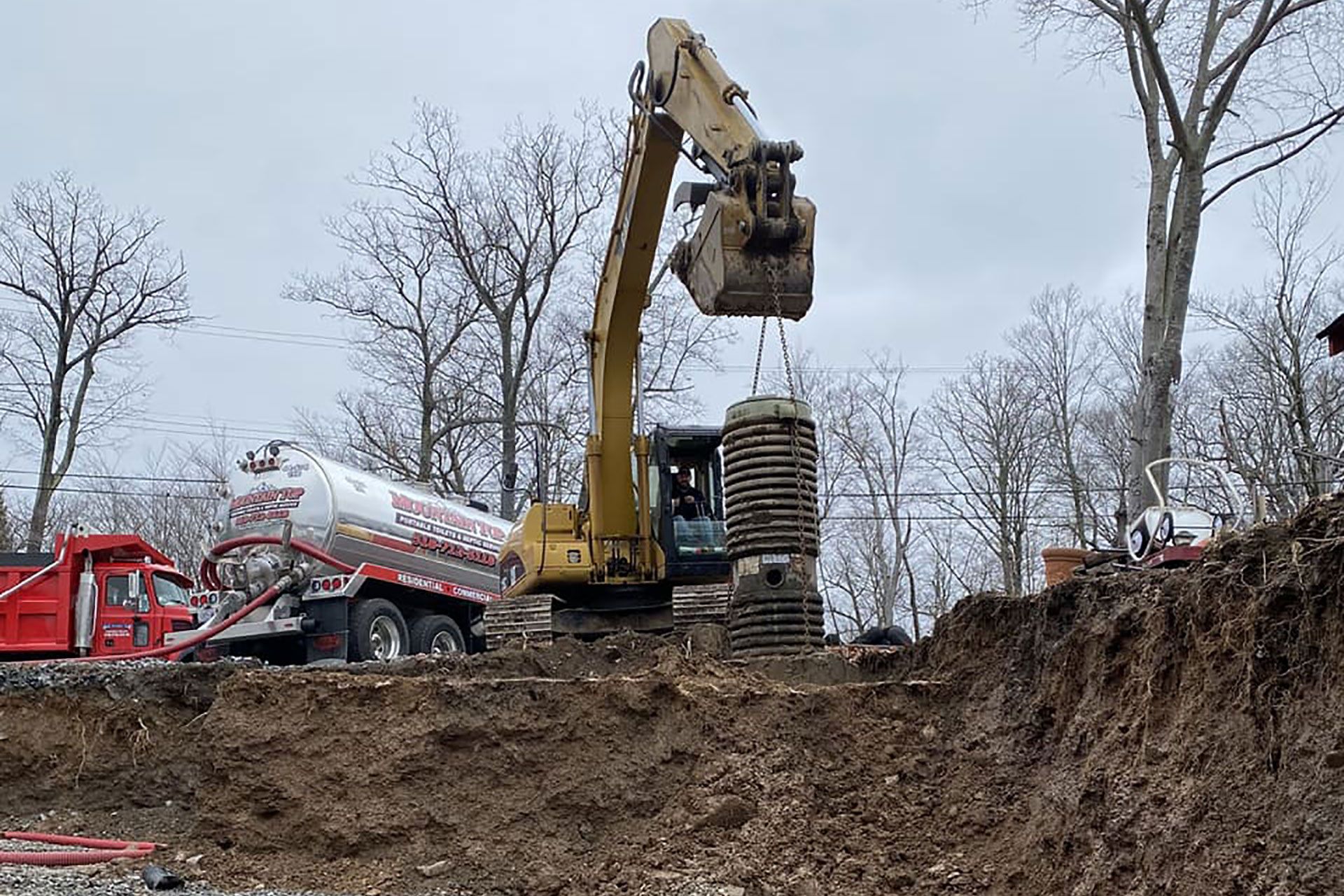 Orange Case excavator digging into a dirt trench, operator in the cab, trees in the background.