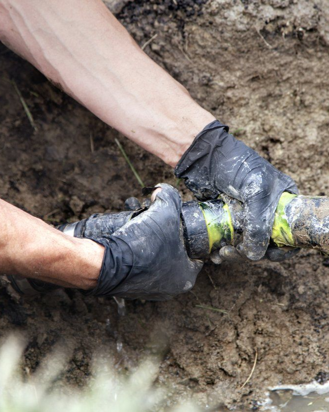 Hands in black gloves connecting a pipe underground.