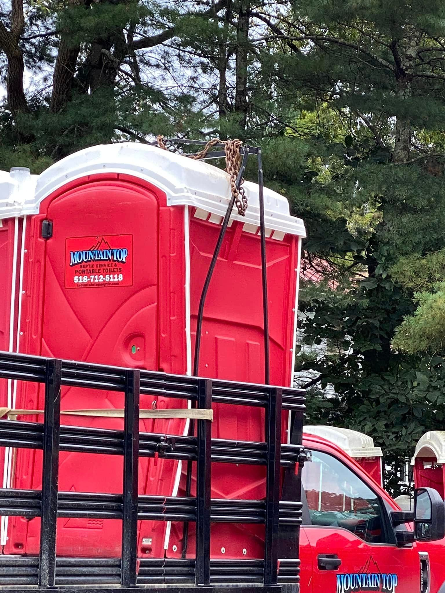 Red portable toilets being lifted by a crane onto a truck bed.