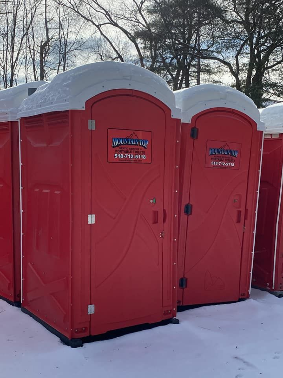 Red portable toilets covered in snow, outdoors.