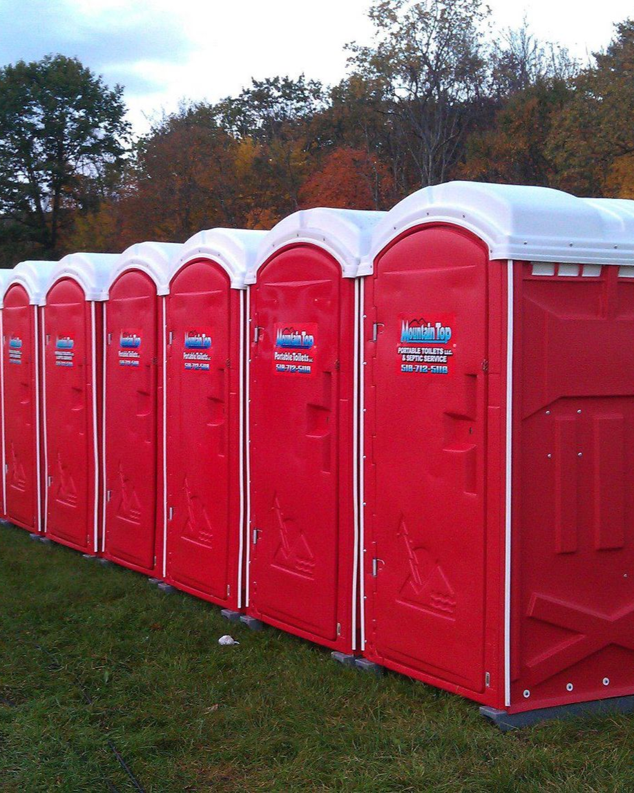 Row of red portable toilets on green grass with fall foliage in the background.