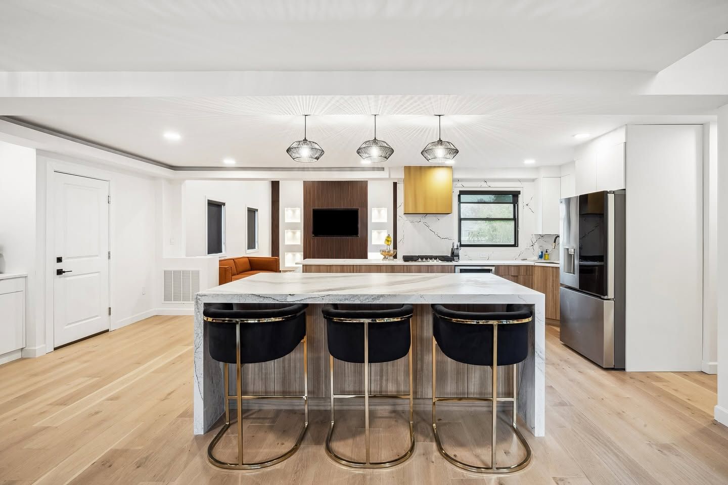 Modern white kitchen with a large island, four black stools, pendant lights, and stainless appliances