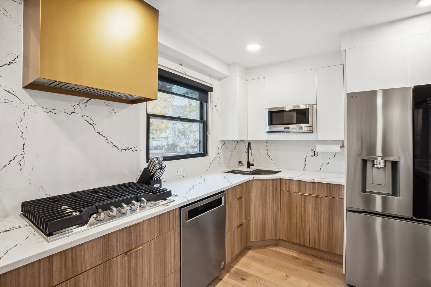 Modern kitchen with wood cabinets, marble countertops, stainless fridge, window, and gas cooktop