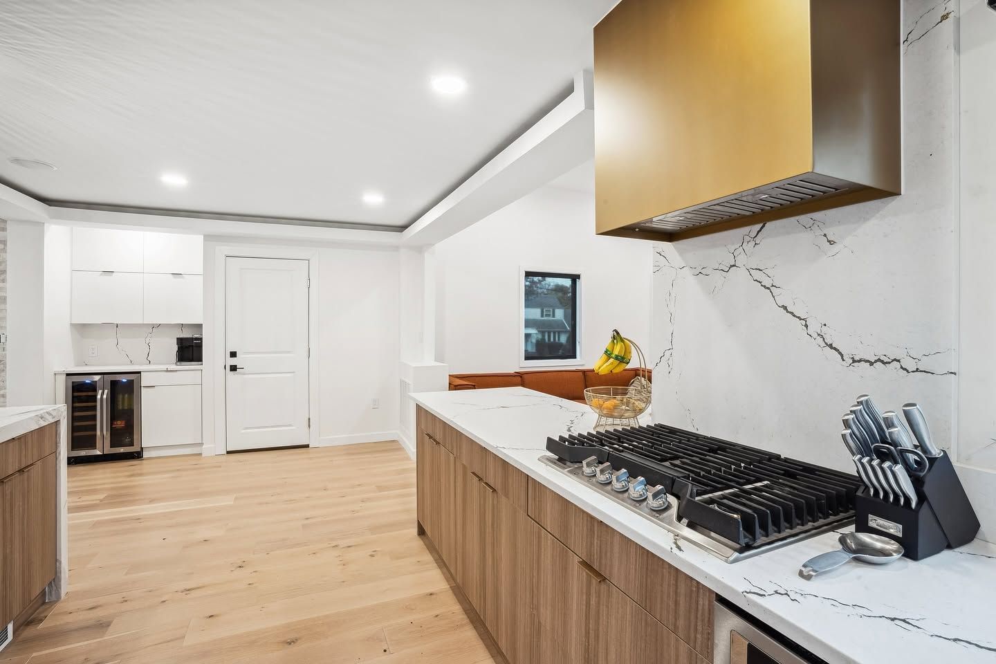 Bright modern kitchen with white cabinets, wood floors, marble counters, and a gas cooktop