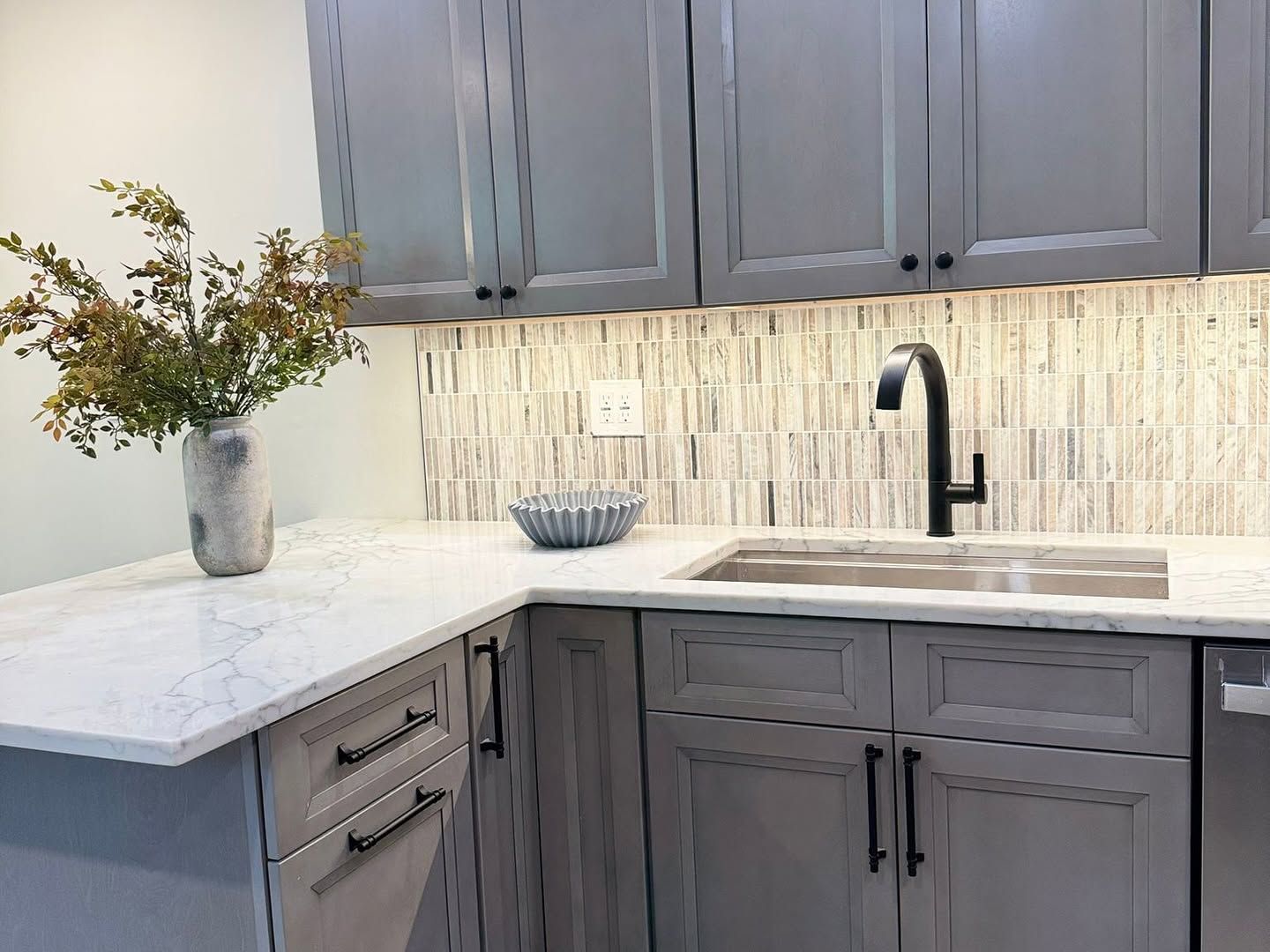 Modern kitchen with gray cabinets, white countertops, sink, and vase of flowers