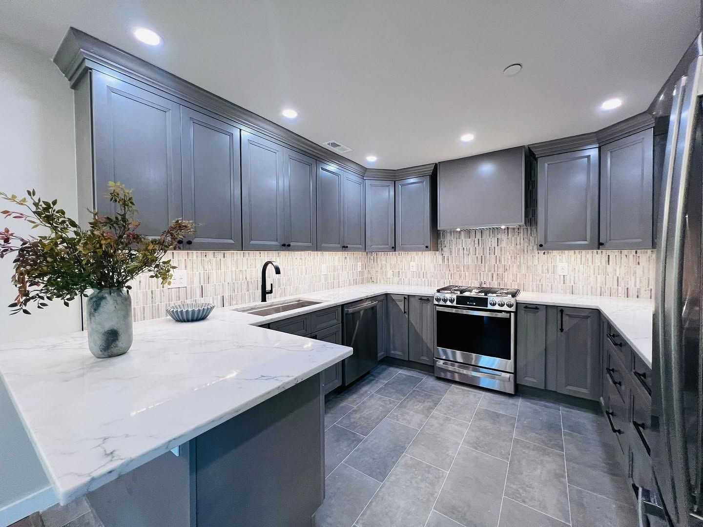Modern gray kitchen with white countertops, stainless stove, tile backsplash, and a vase of flowers on the island