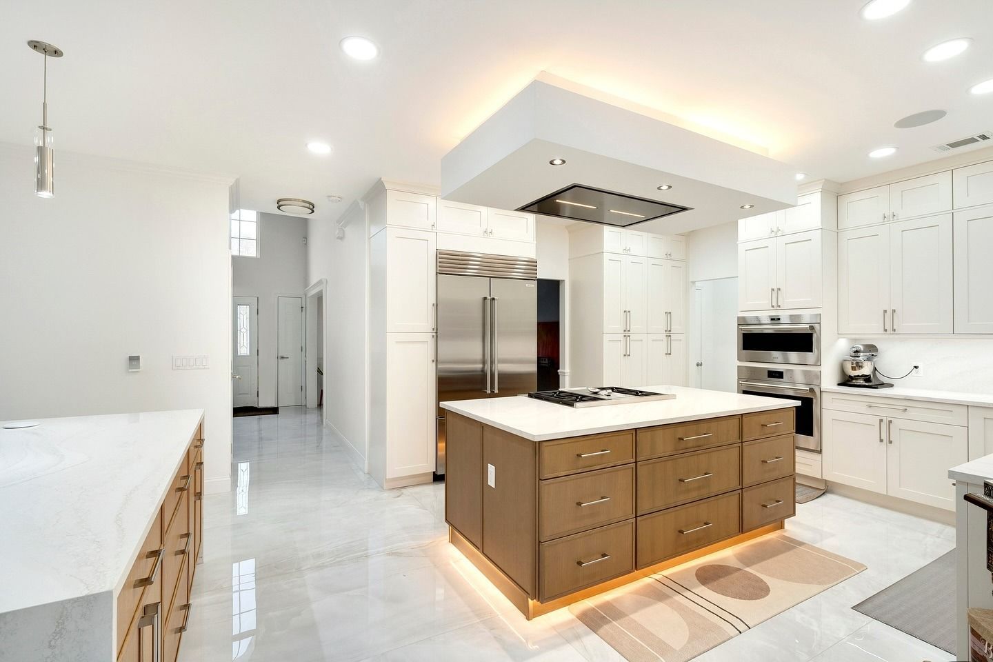 Bright modern kitchen with white cabinetry, stainless appliances, and a large central island with warm underlighting