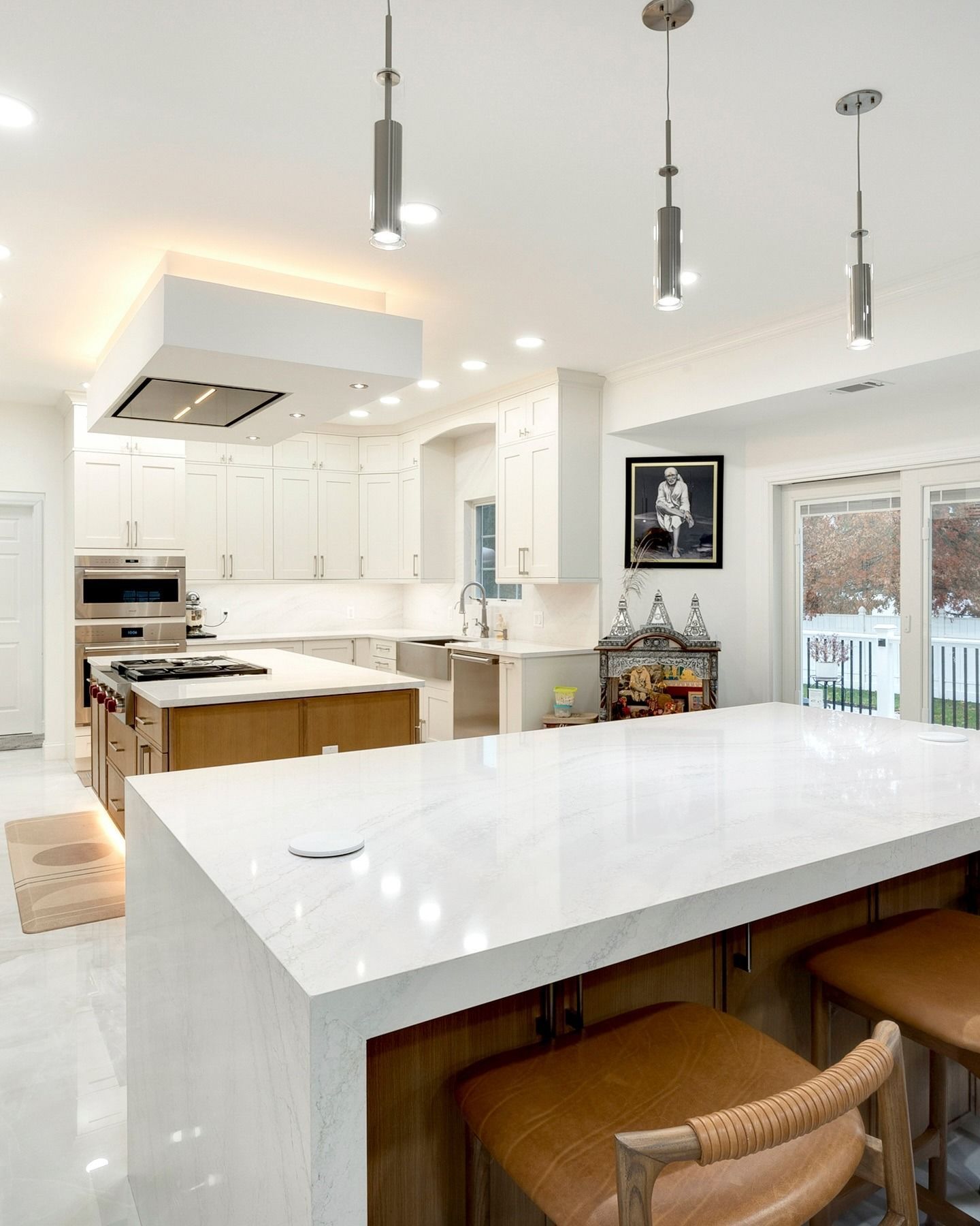 Bright modern kitchen with white cabinets, marble island, pendant lights, and a view of the backyard