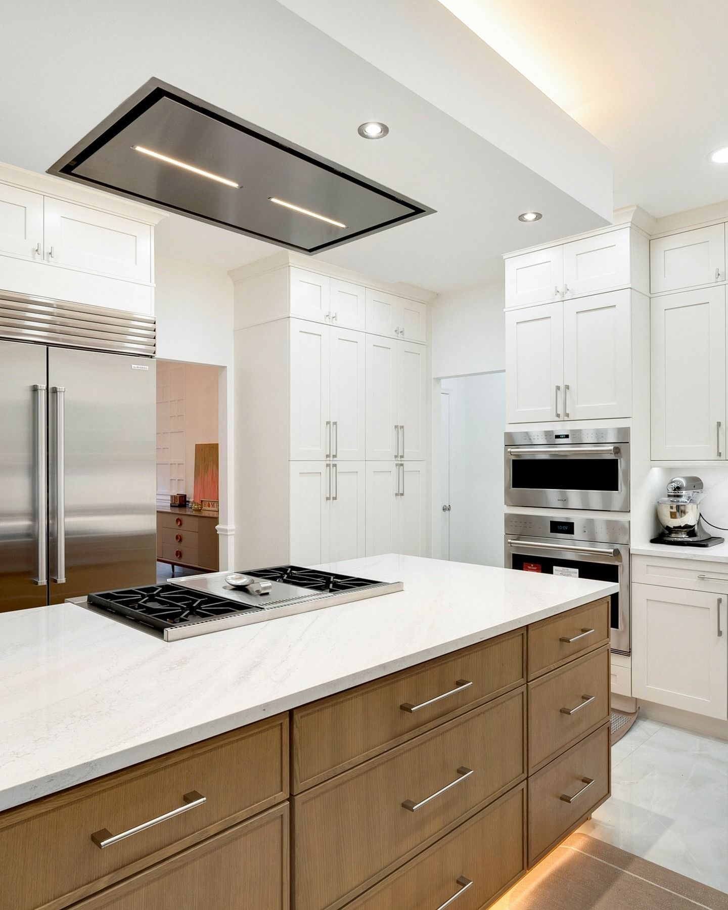 Bright modern kitchen with white cabinets, stainless appliances, and a wood island with a cooktop.