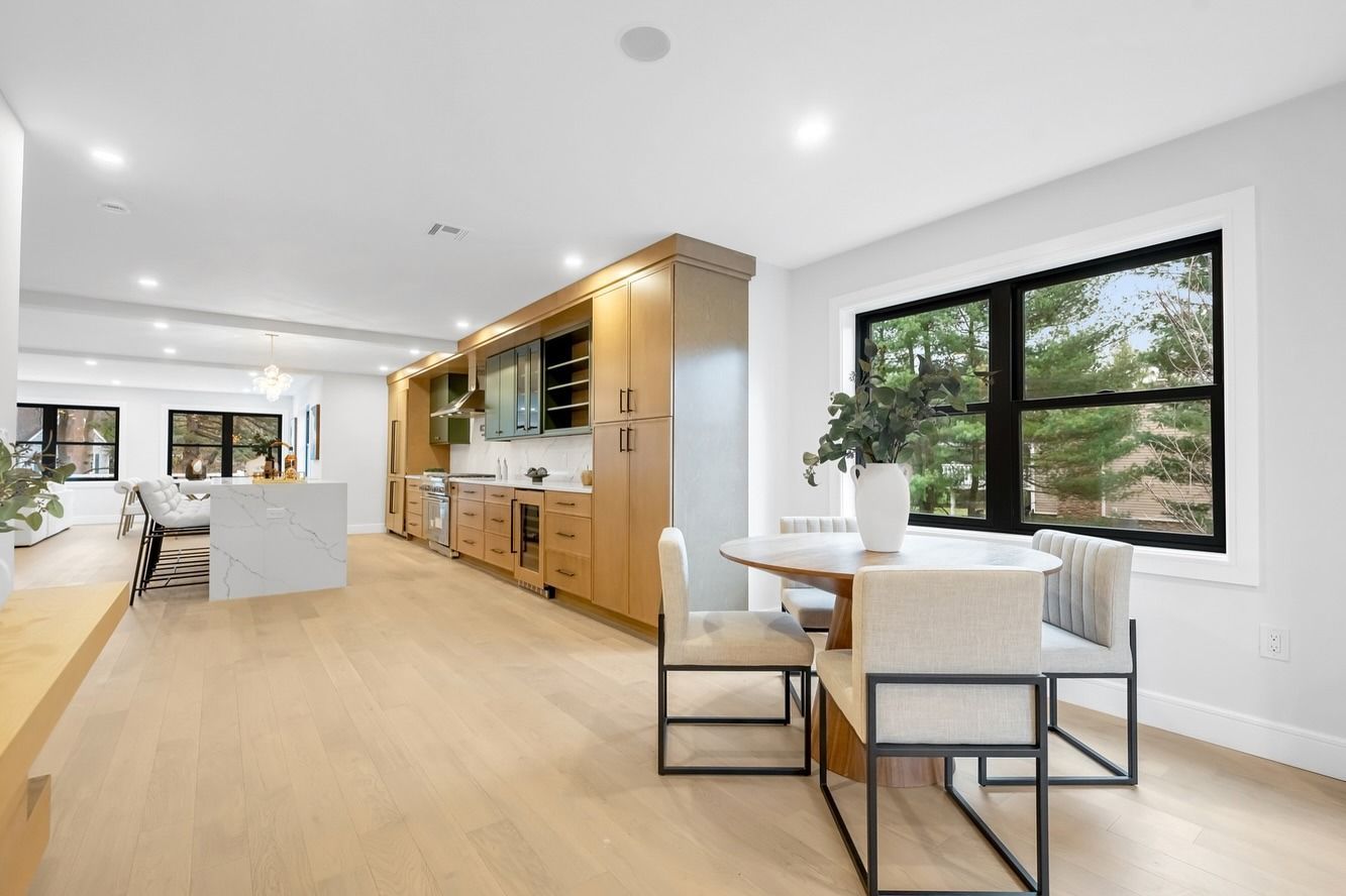 Bright open kitchen and dining area with light wood floors, white walls, and large windows.