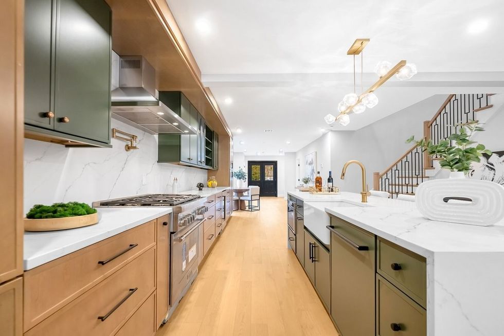 Bright modern kitchen with wood cabinets, central island, and staircase in the background