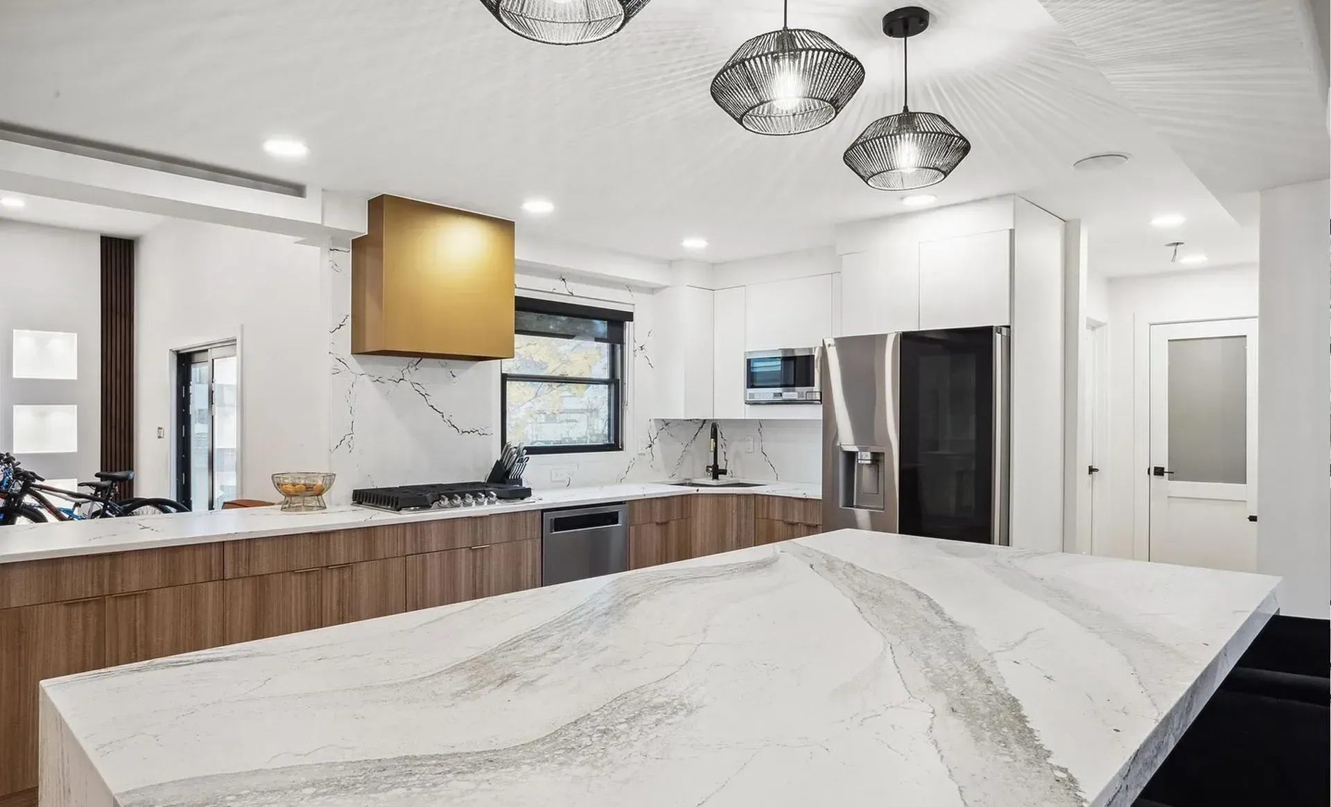 Bright modern kitchen with white island, wood cabinetry, pendant lights, and stainless appliances
