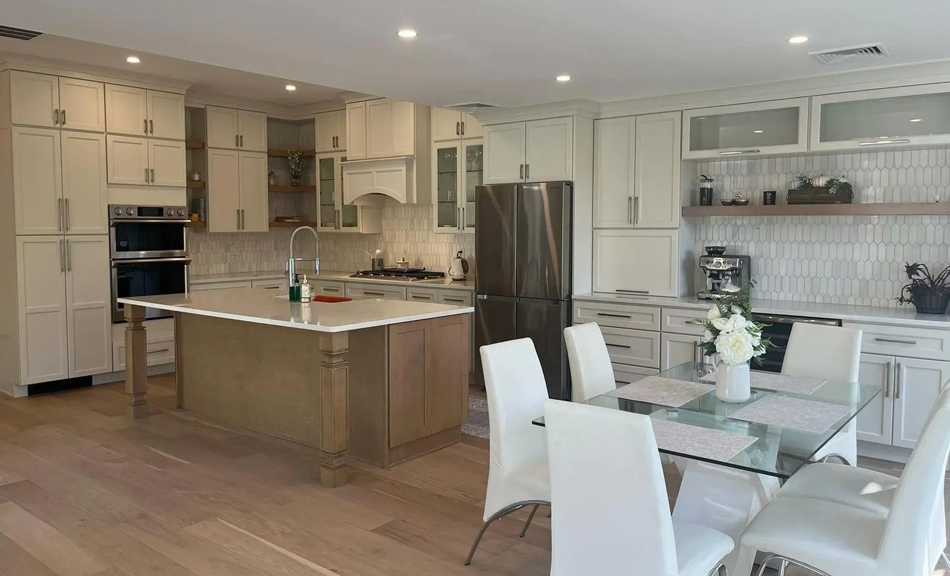Bright modern kitchen with island, stainless steel appliances, and white dining chairs beside a glass table