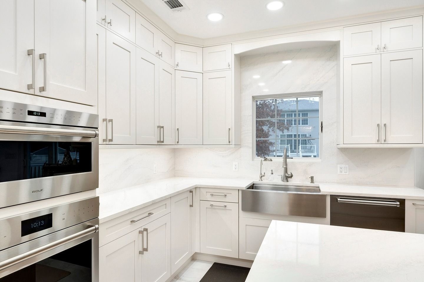 Bright white modern kitchen with stainless steel appliances and a large sink under a window