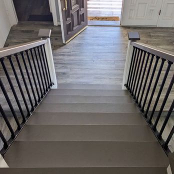 Front view down a staircase with black railings leading to a hallway and doorway beyond.
