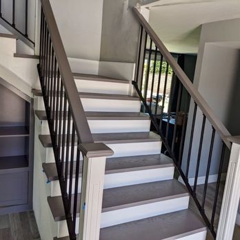 Indoor staircase with gray carpeted steps and black metal railing beside white walls.