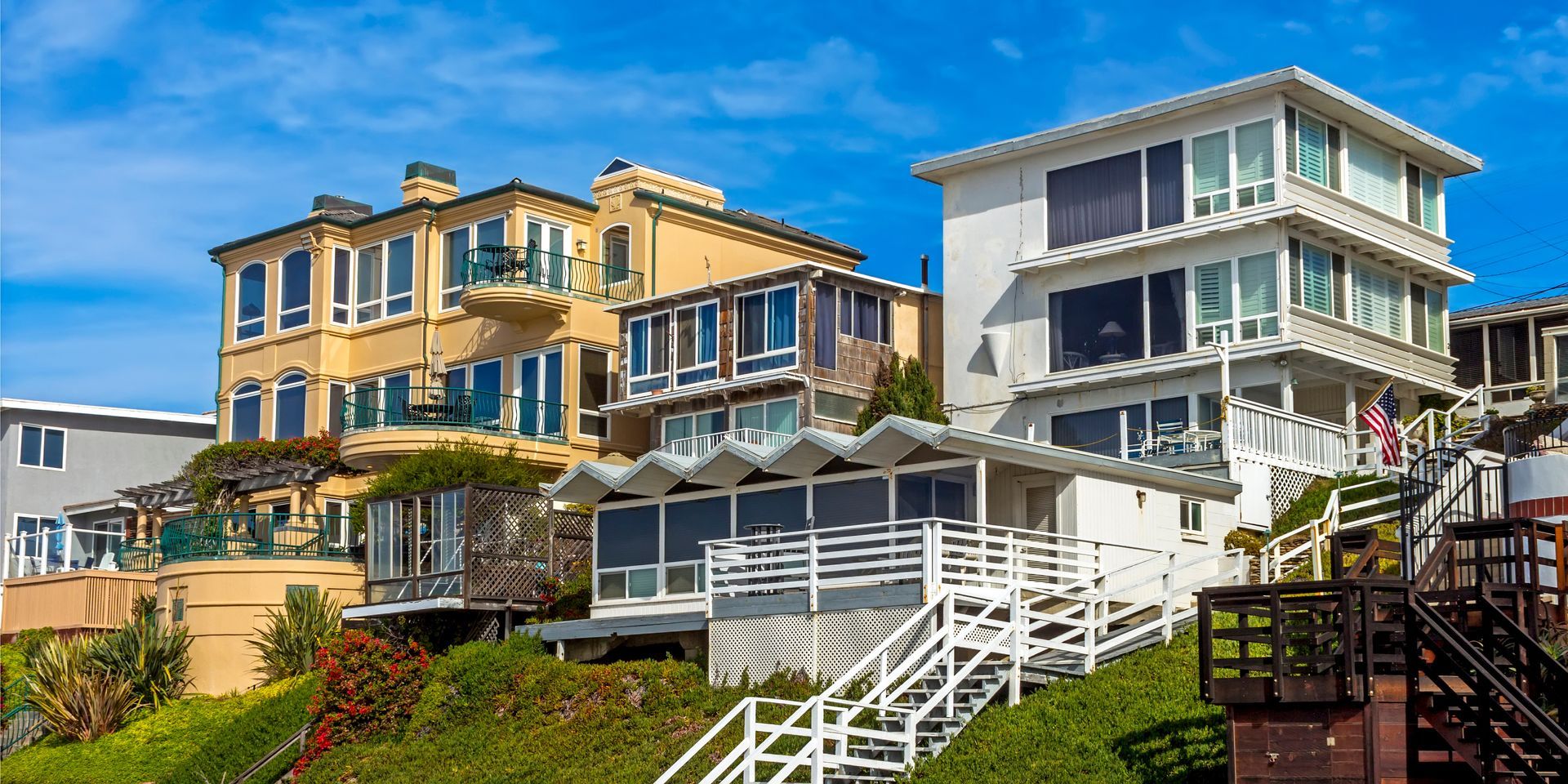 Colorful seaside houses with balconies on a sunny hillside, with ocean views and white railings