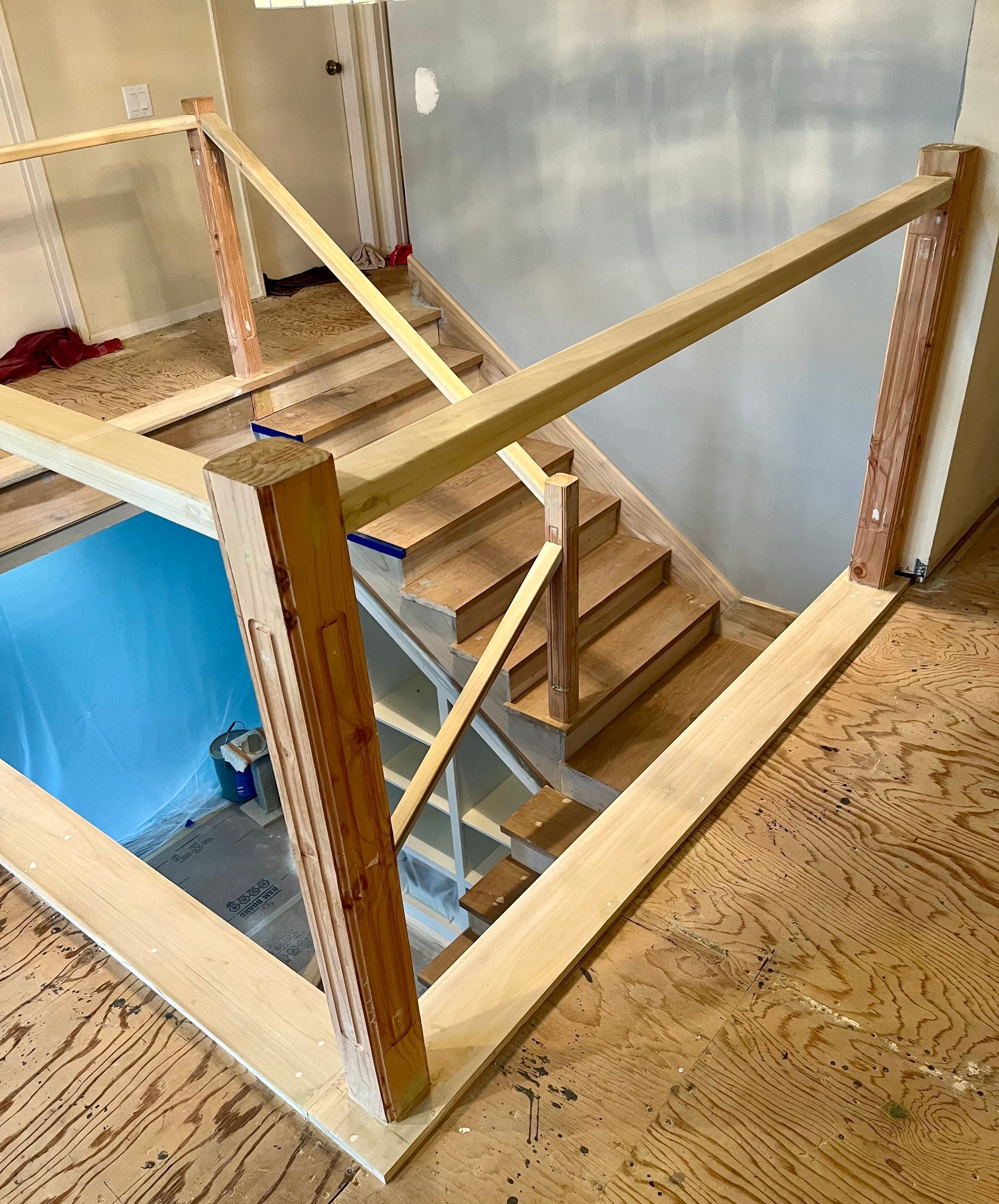Wooden staircase with handrails in a workshop, seen from above on a plywood floor.