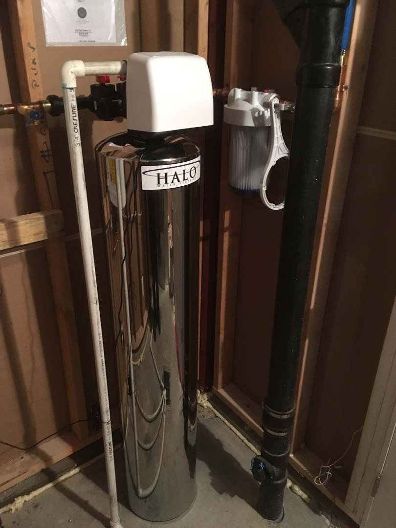 Water filtration system in a utility closet with a large shiny tank, a filter, and piping.