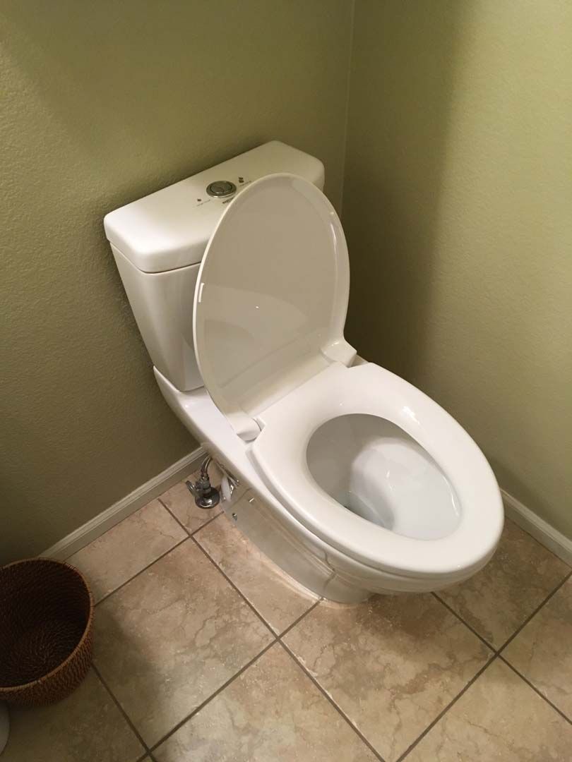 White toilet with open lid in a bathroom corner, beige tiled floor, and light green wall.