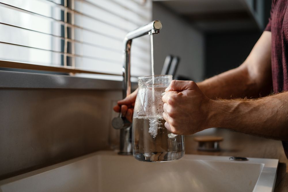 Person filling a clear pitcher with water from a faucet in a kitchen sink.