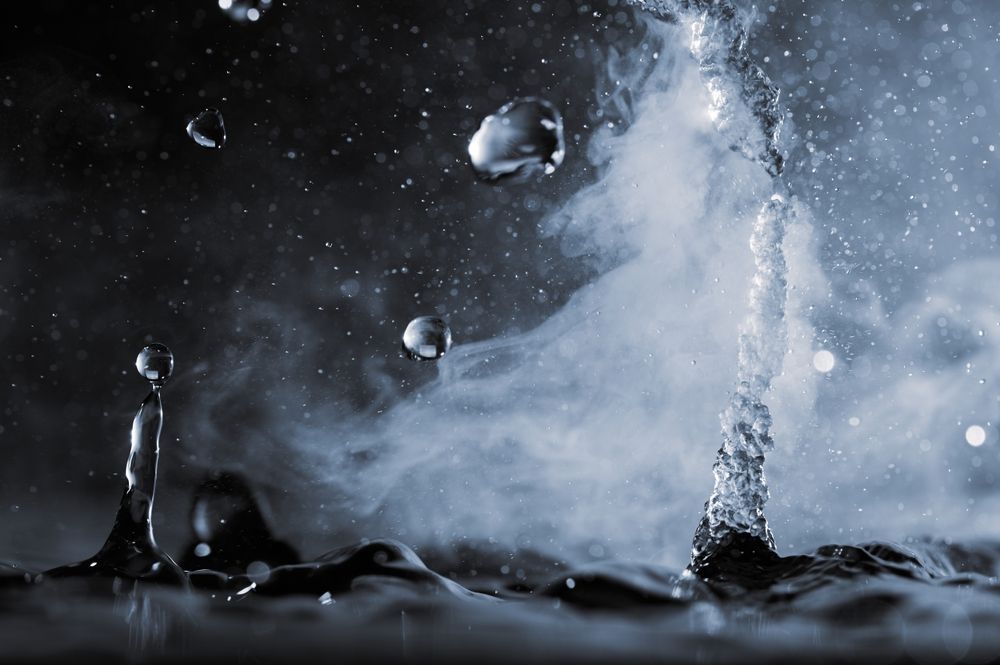 Water droplets and a stream of water with vapor in a dark setting.