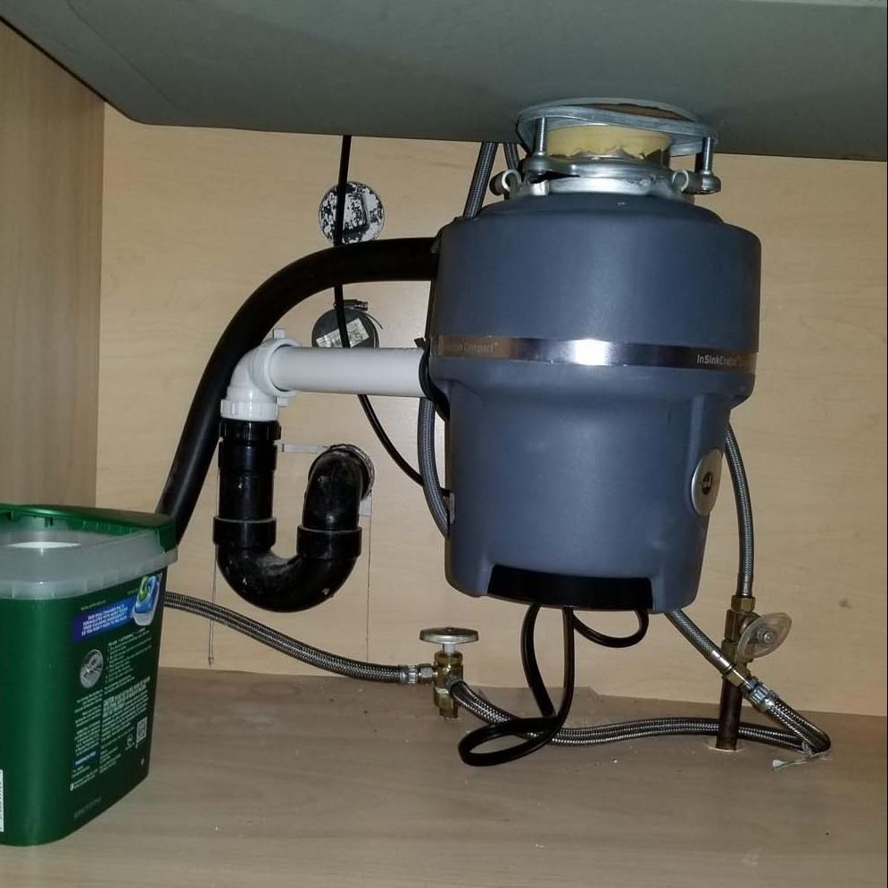 Garbage disposal unit under a sink with plumbing and drain cleaner container.