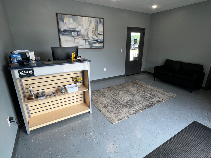 Modern office lobby with a reception desk, gray rug, black couch, and glass door | Campbell Automotive