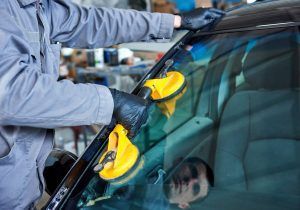 Person cleaning a car windshield with yellow cloths in a garage