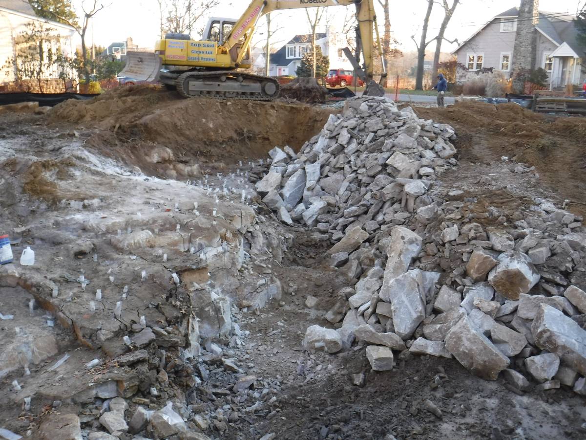 Construction site with excavator digging; piles of rubble and dirt.