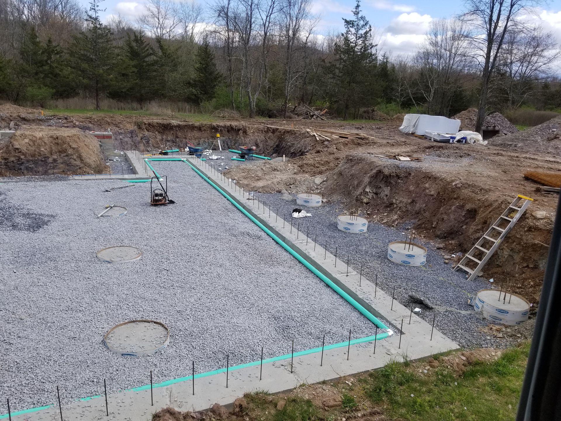 Construction site with concrete foundation and gravel base. Trenches and plumbing visible.