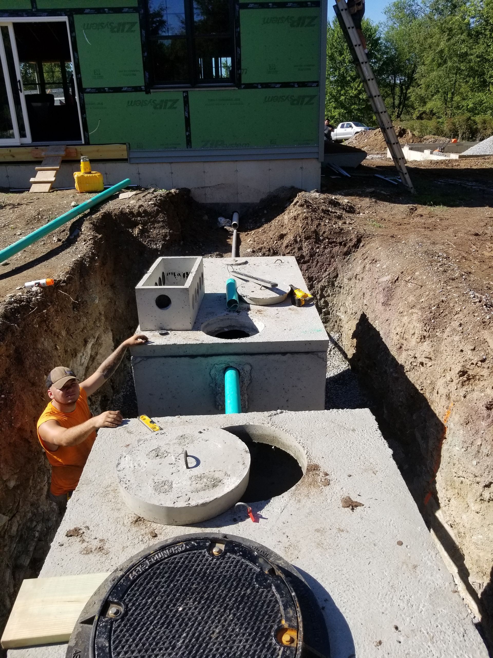 Construction worker with septic tanks in a trench near a building.