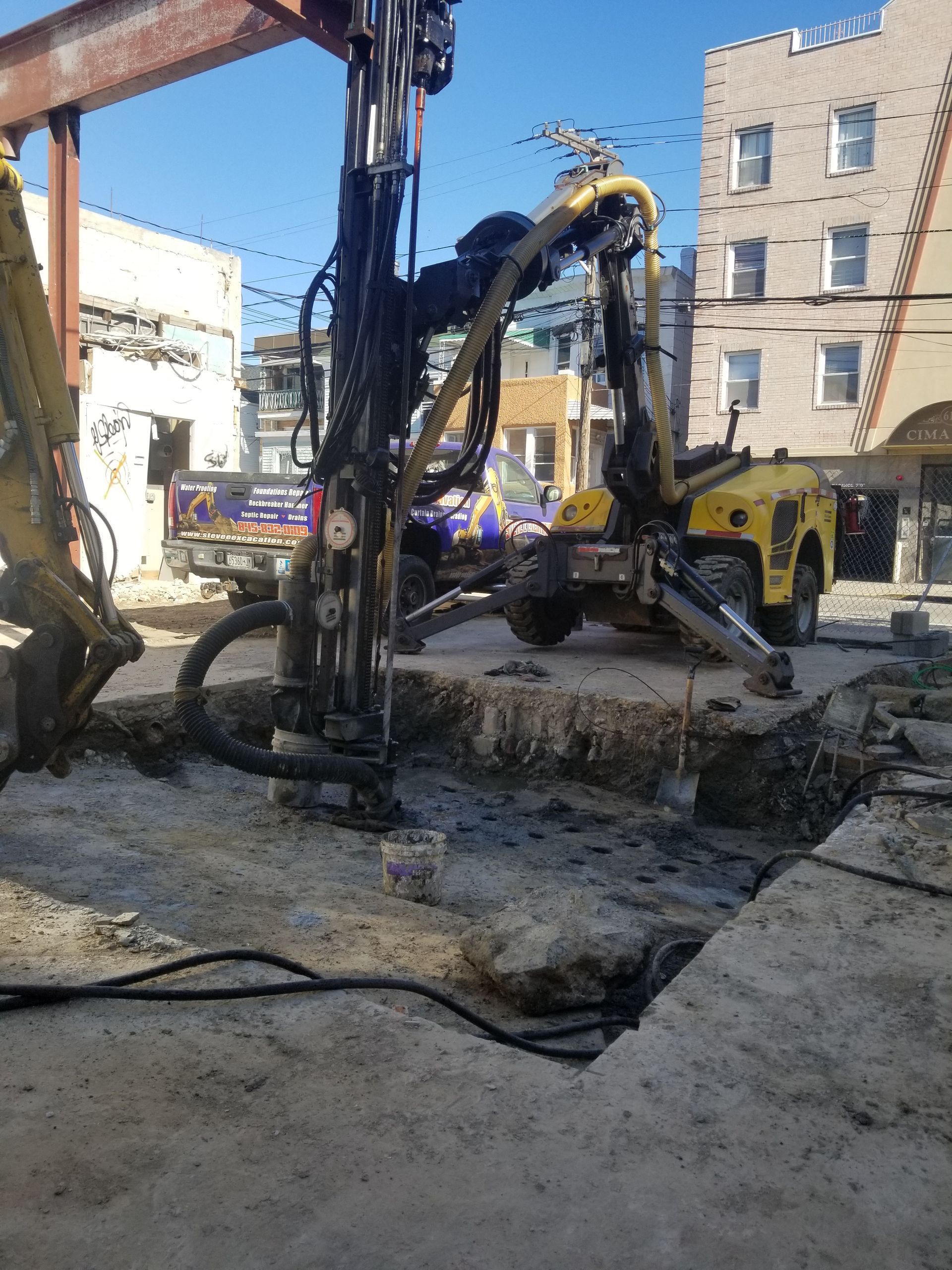Construction site with drilling equipment extracting material from a large hole in concrete.