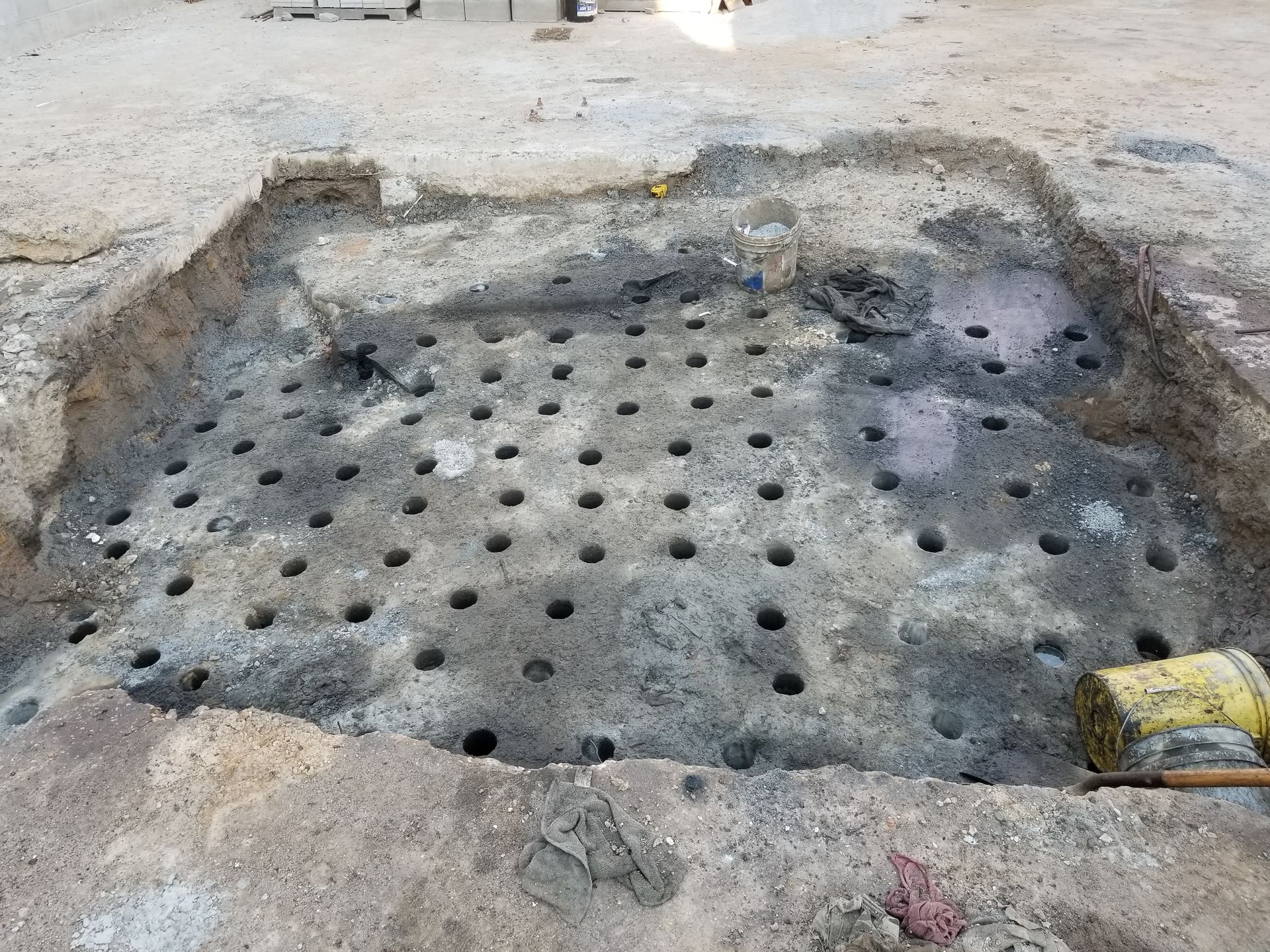 Ground surface with numerous evenly spaced holes, possibly for construction or repair work.