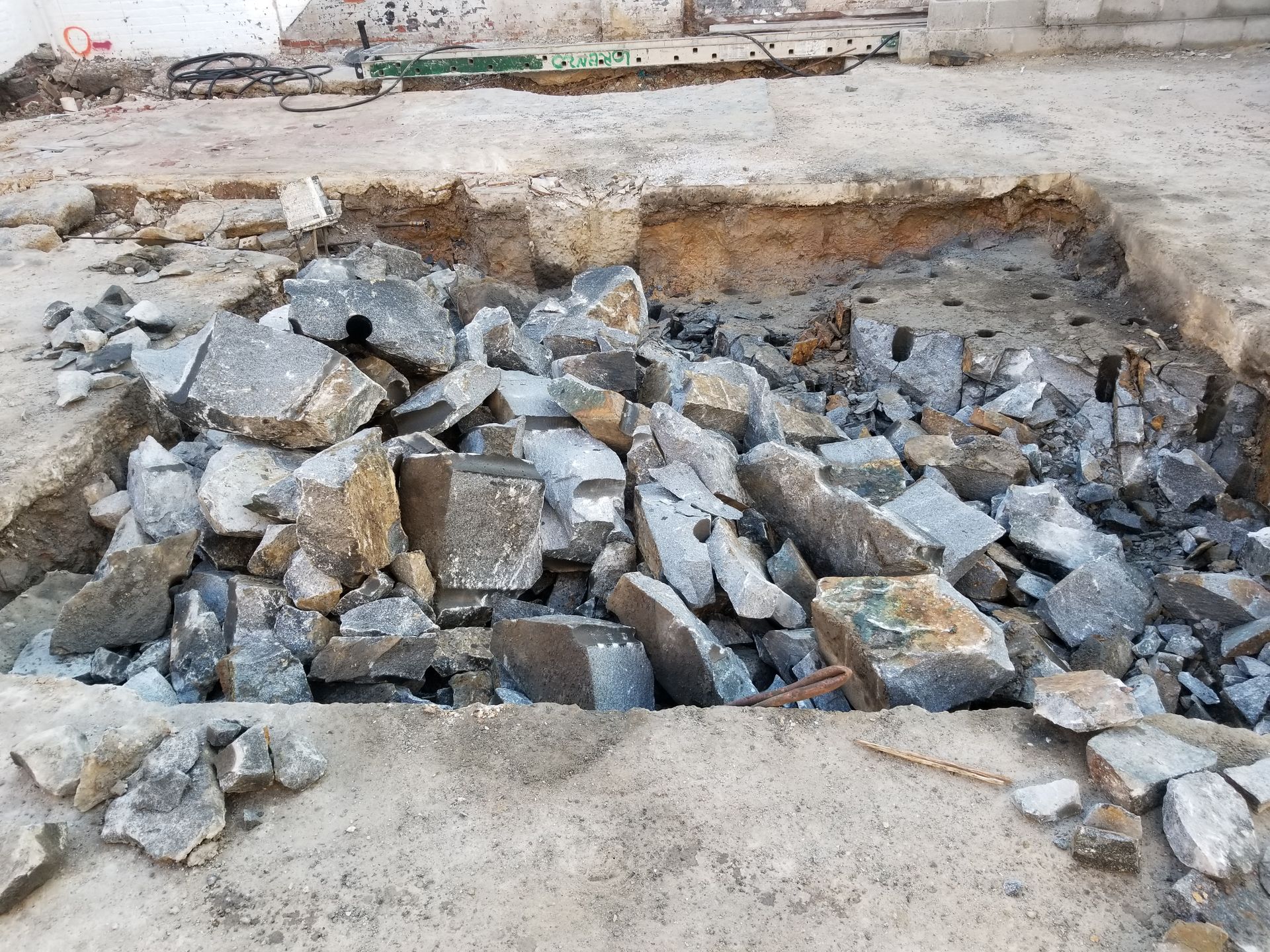 Pile of broken concrete debris inside a rectangular excavation, showing a construction site.