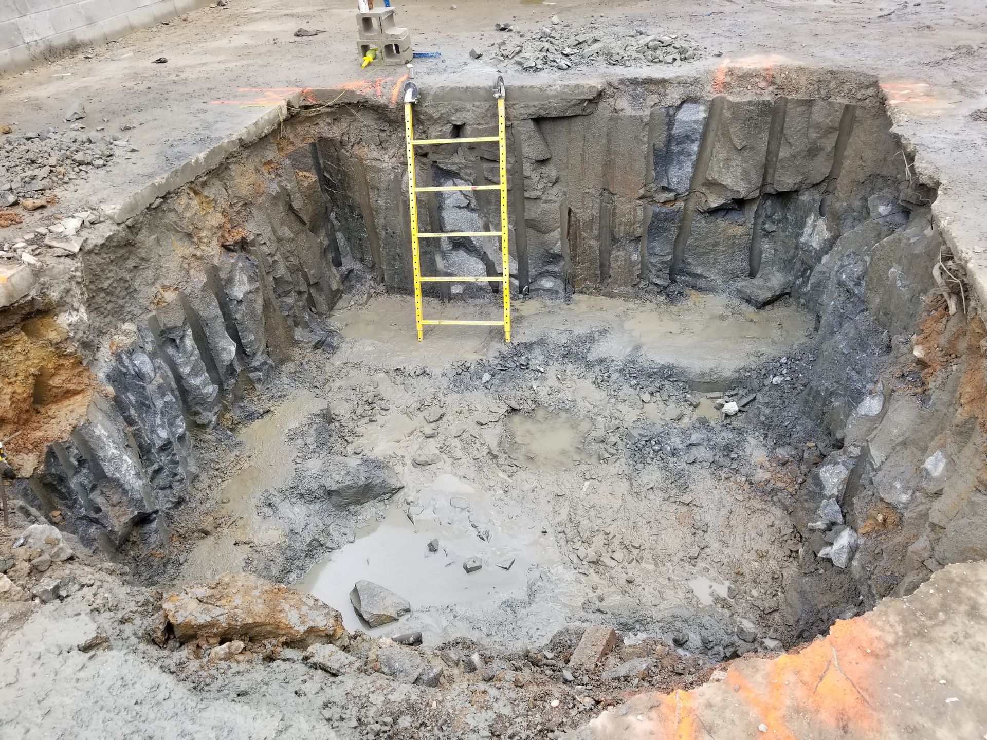 Open excavated pit with a yellow ladder inside.