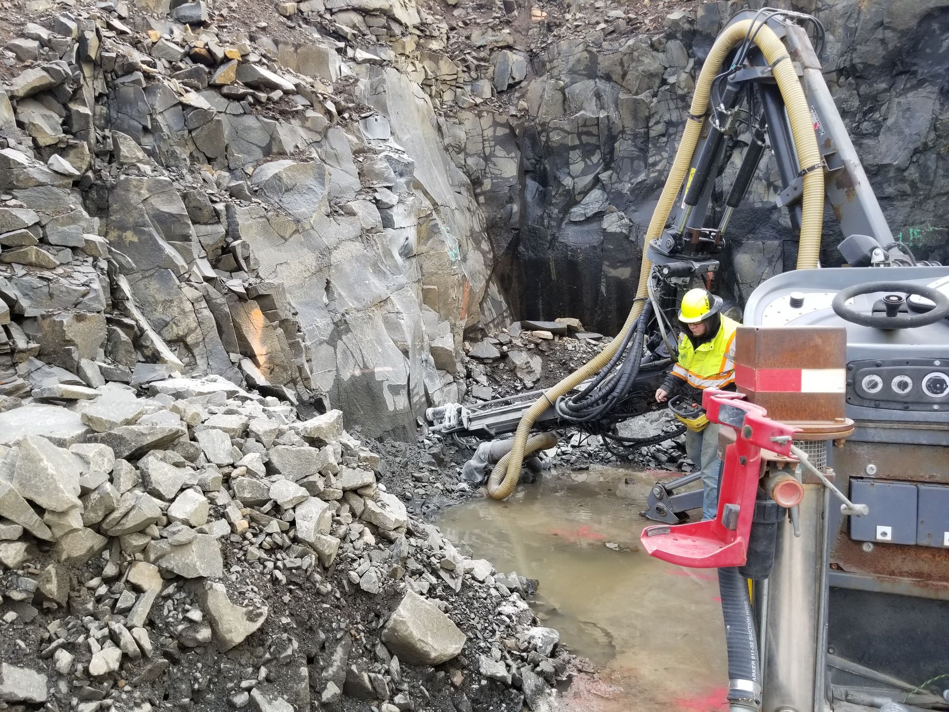 A worker operates drilling machinery in a rock quarry.
